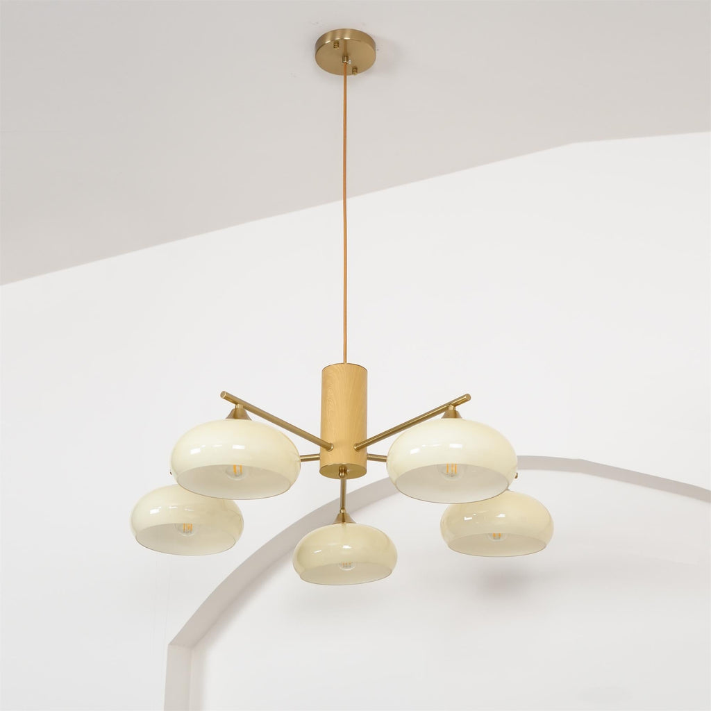 Full drop of the Clérachic chandelier, from the brass ceiling canopy down the cord to five lit beige glass shades.