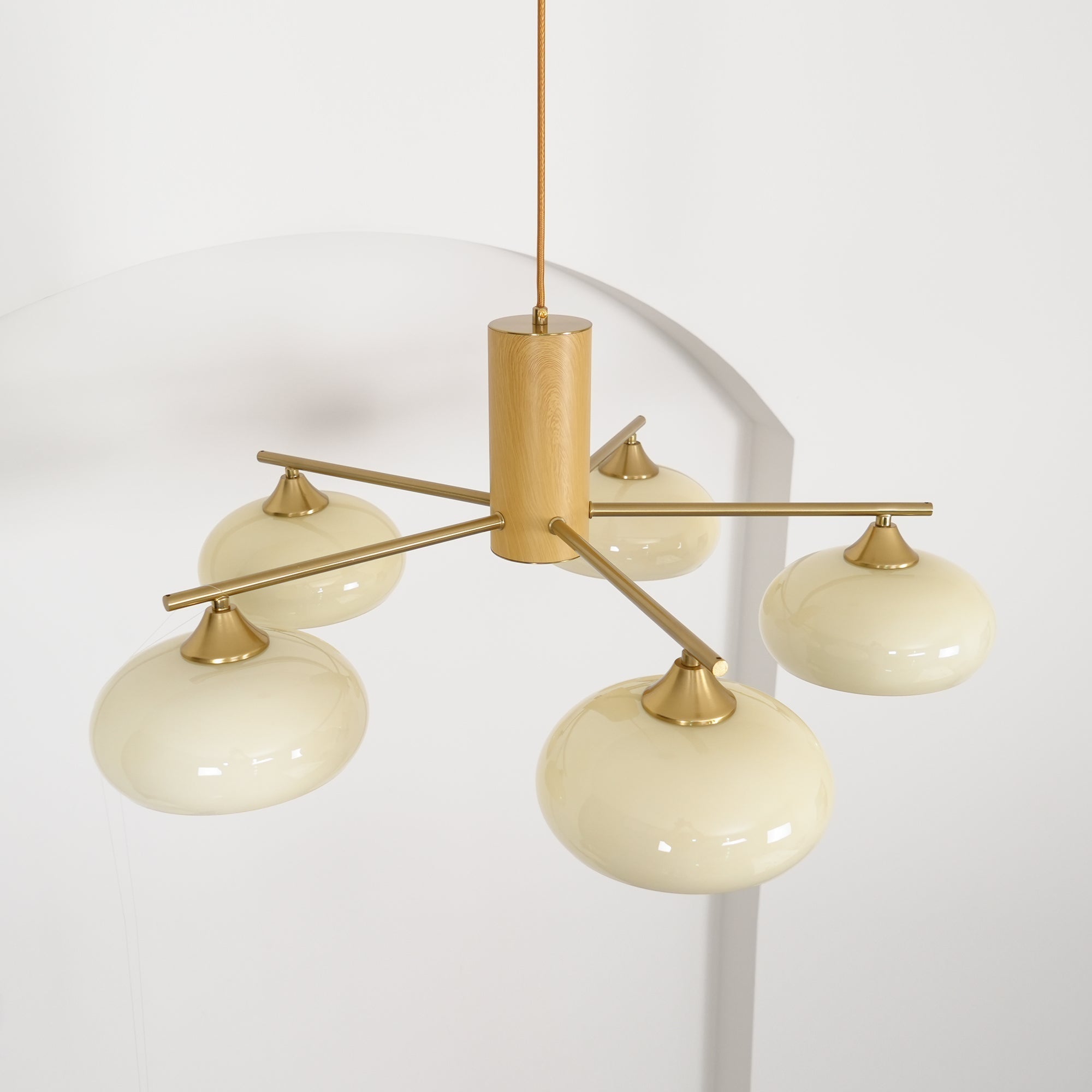 Brass rods cross through the wood cylinder of the Clérachic chandelier, holding five beige shades at two heights.