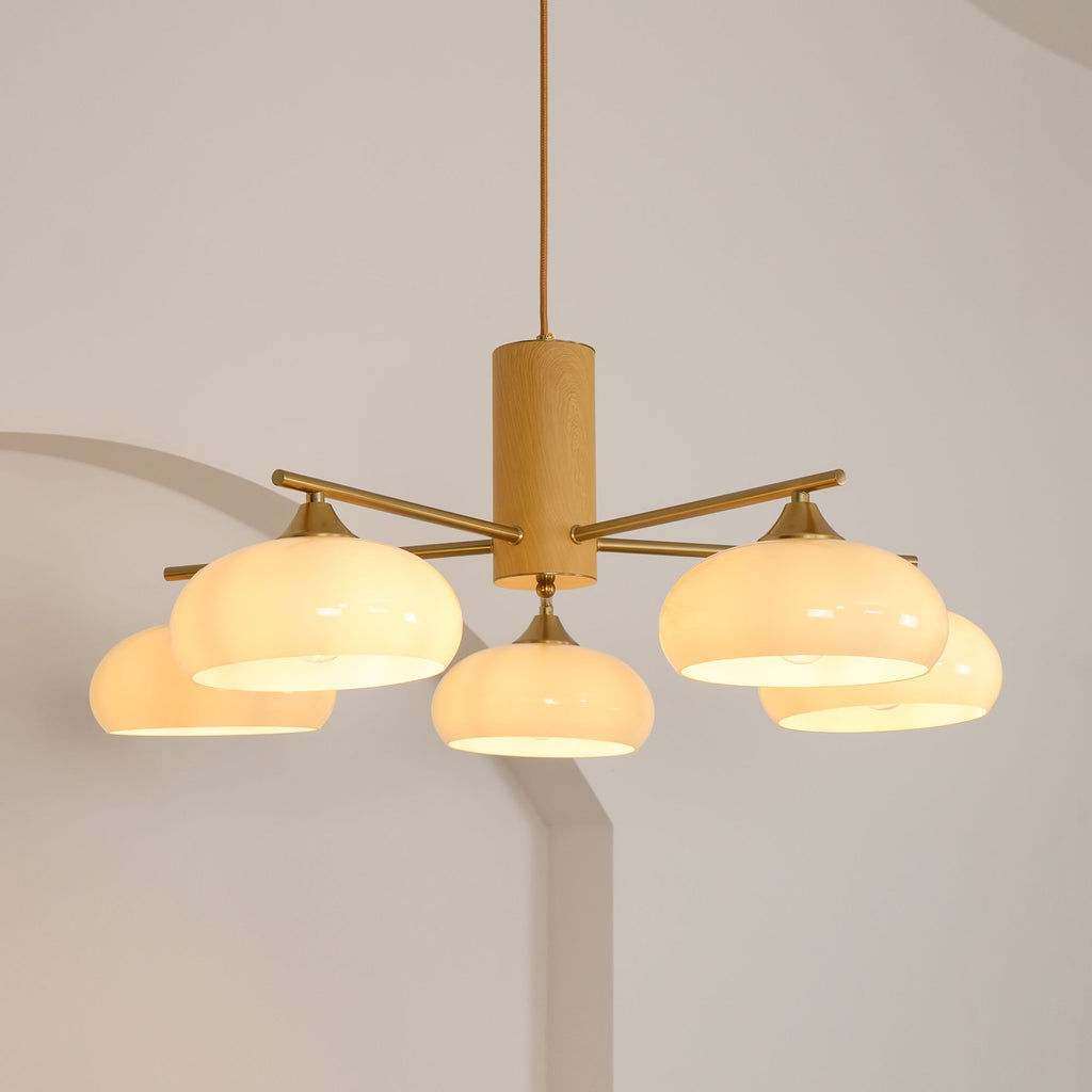 Warm light spills from the five white glass shades of the Clérachic wood and brass chandelier, seen from below.