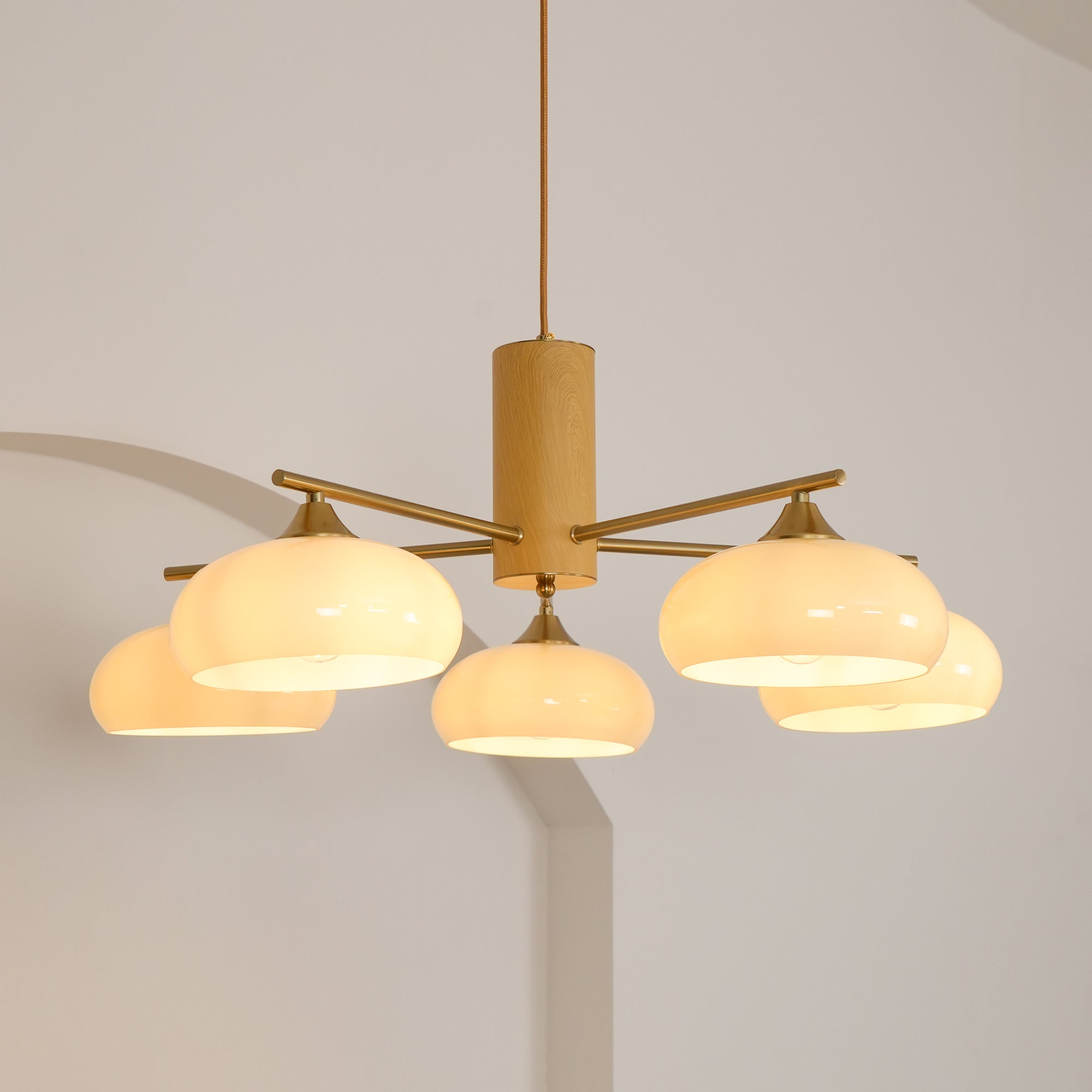 Warm light spills from the five white glass shades of the Clérachic wood and brass chandelier, seen from below.
