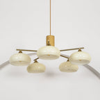 Lit from within, the Clérachic chandelier shows one beige glass shade set higher than the four ranged around it.