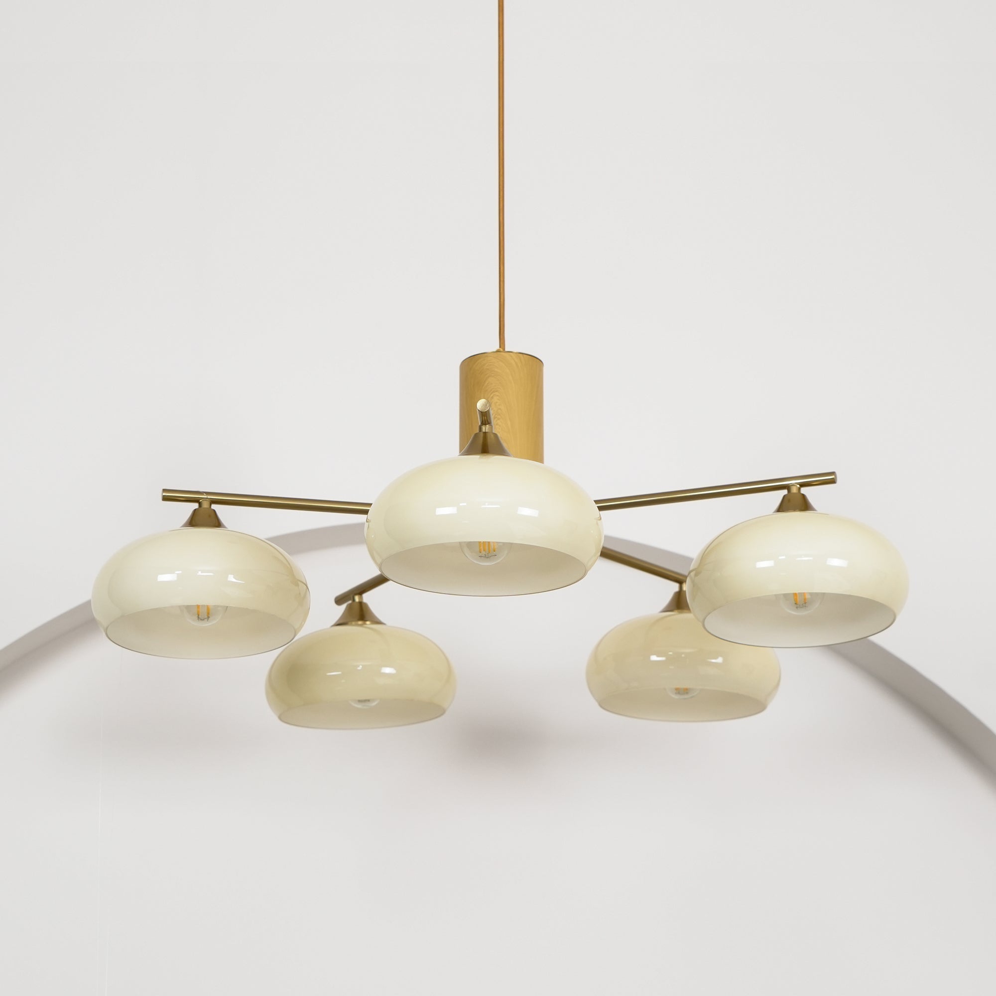 Lit from within, the Clérachic chandelier shows one beige glass shade set higher than the four ranged around it.