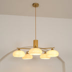 Long cord and brass canopy above the Clérachic five-light chandelier, its white glass shades lit in a studio.