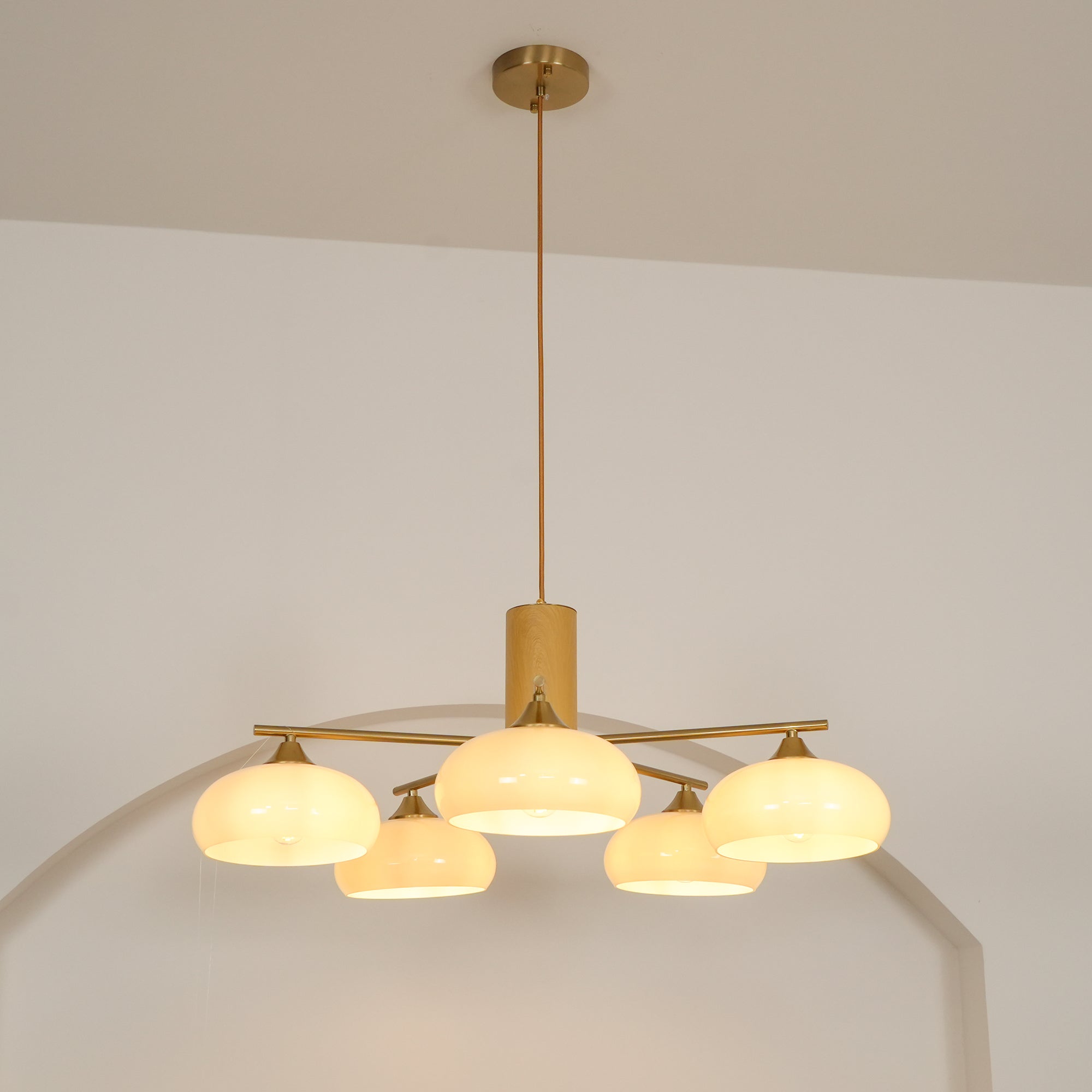 Long cord and brass canopy above the Clérachic five-light chandelier, its white glass shades lit in a studio.