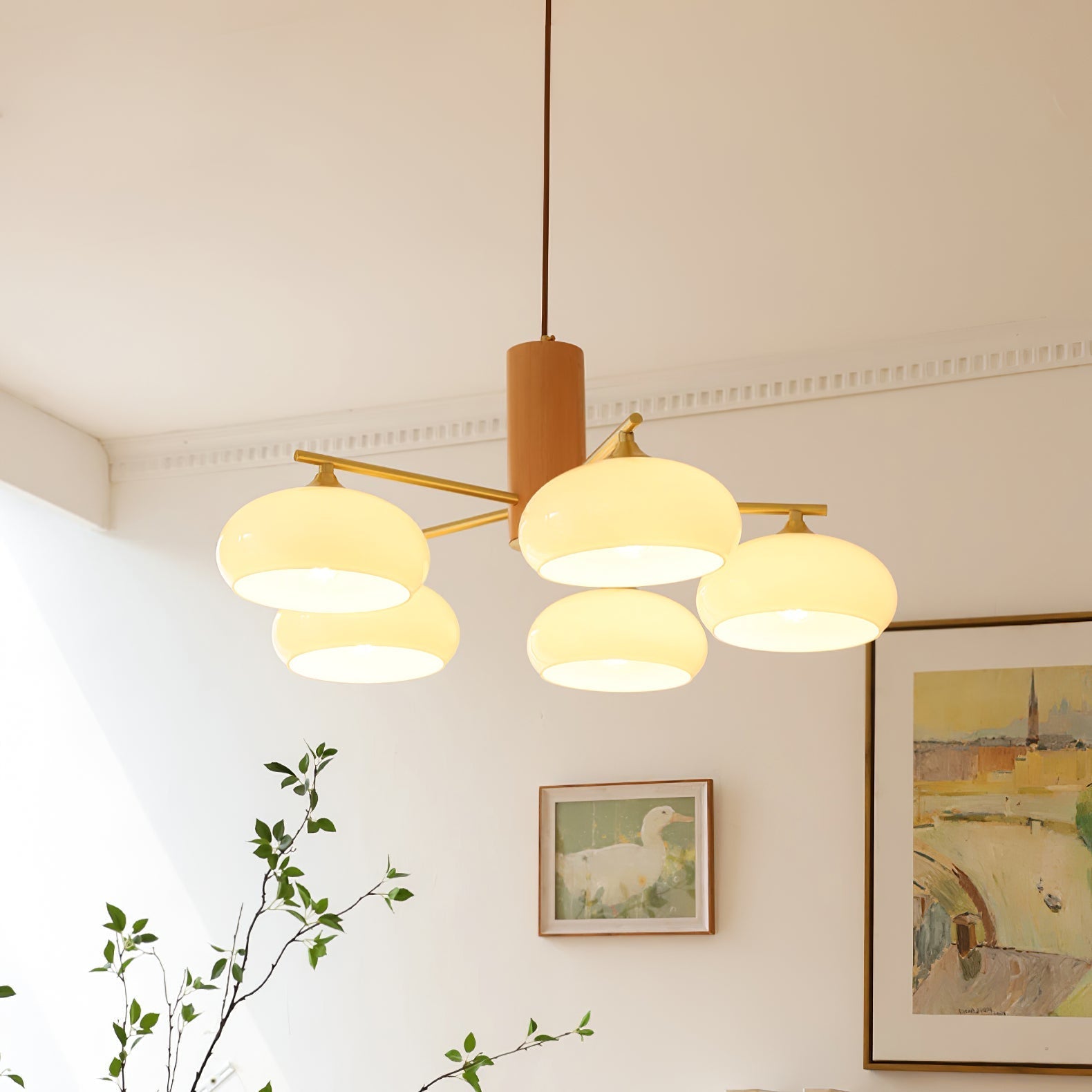 The Clérachic chandelier fills a corner with beige glass warmth above framed paintings and a slim green branch.