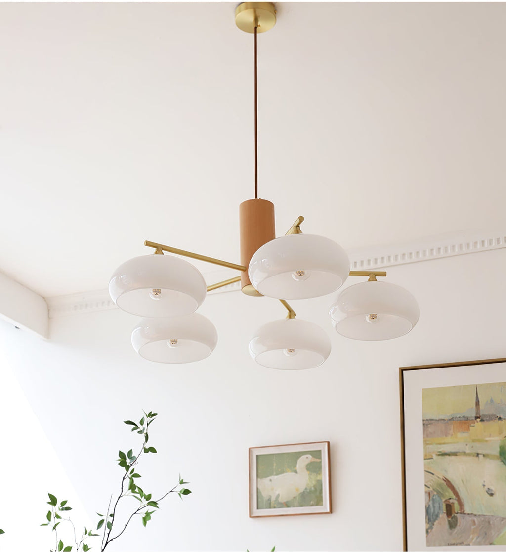 Five white glass shades of the Clérachic chandelier glow softly below a cornice in a bright, art-hung room.