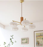 Five white glass shades of the Clérachic chandelier glow softly below a cornice in a bright, art-hung room.