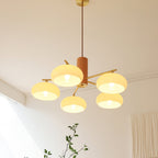 Beige glass shades of the Clérachic chandelier catch the daylight in a room corner with curtain and plant.