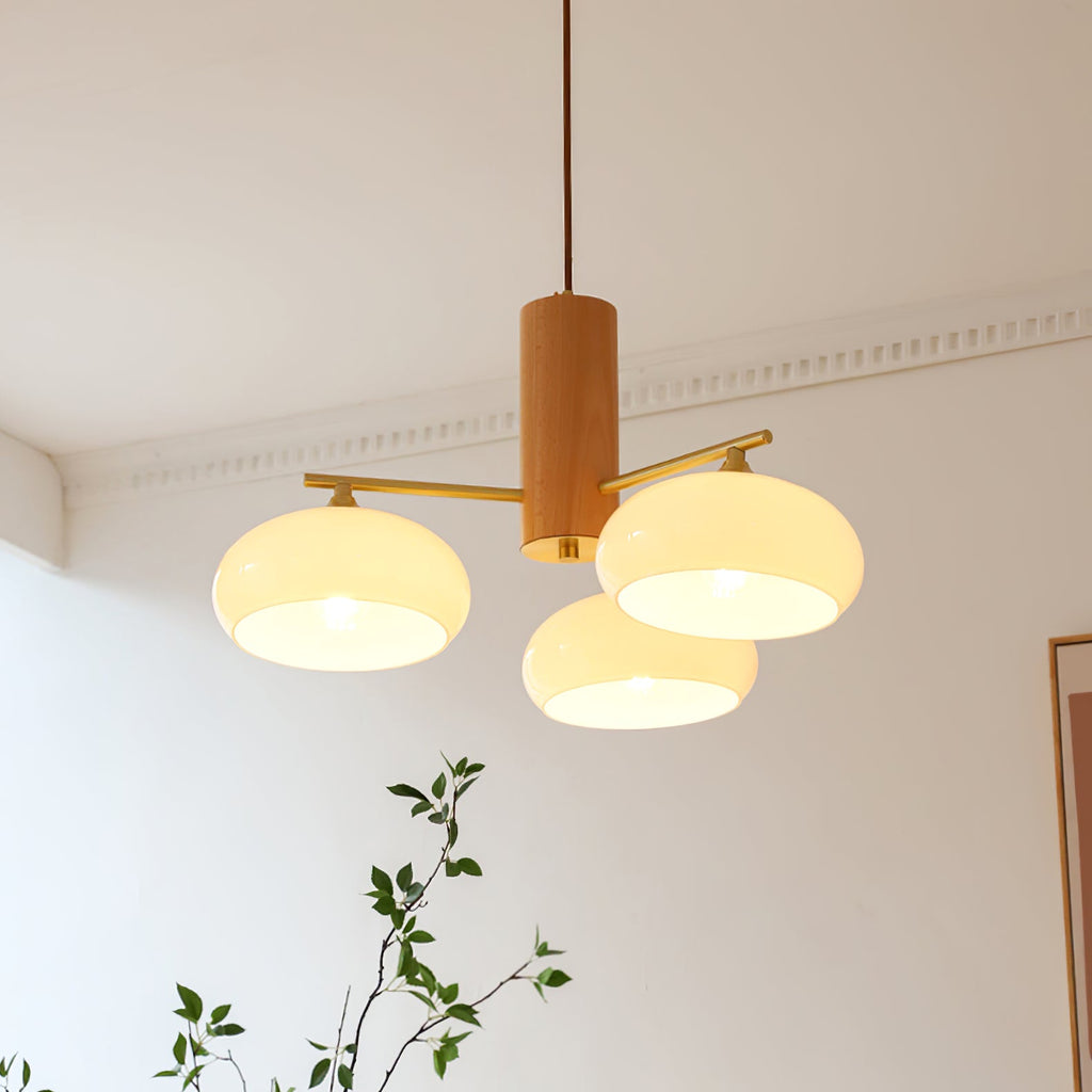 The three-light Clérachic chandelier lit in beige glass, tucked into a room corner above a leafy branch.