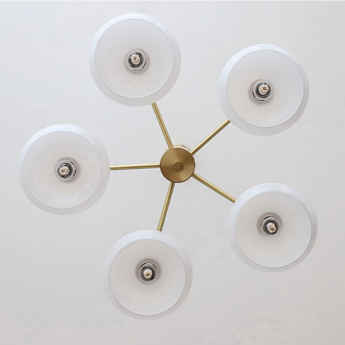 Underside view of the Clérachic five-light chandelier, white glass discs radiating from the brass centre hub.
