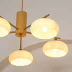 Detail of the Clérachic chandelier's brass cone fitters and wood body with five beige shades lit around it.