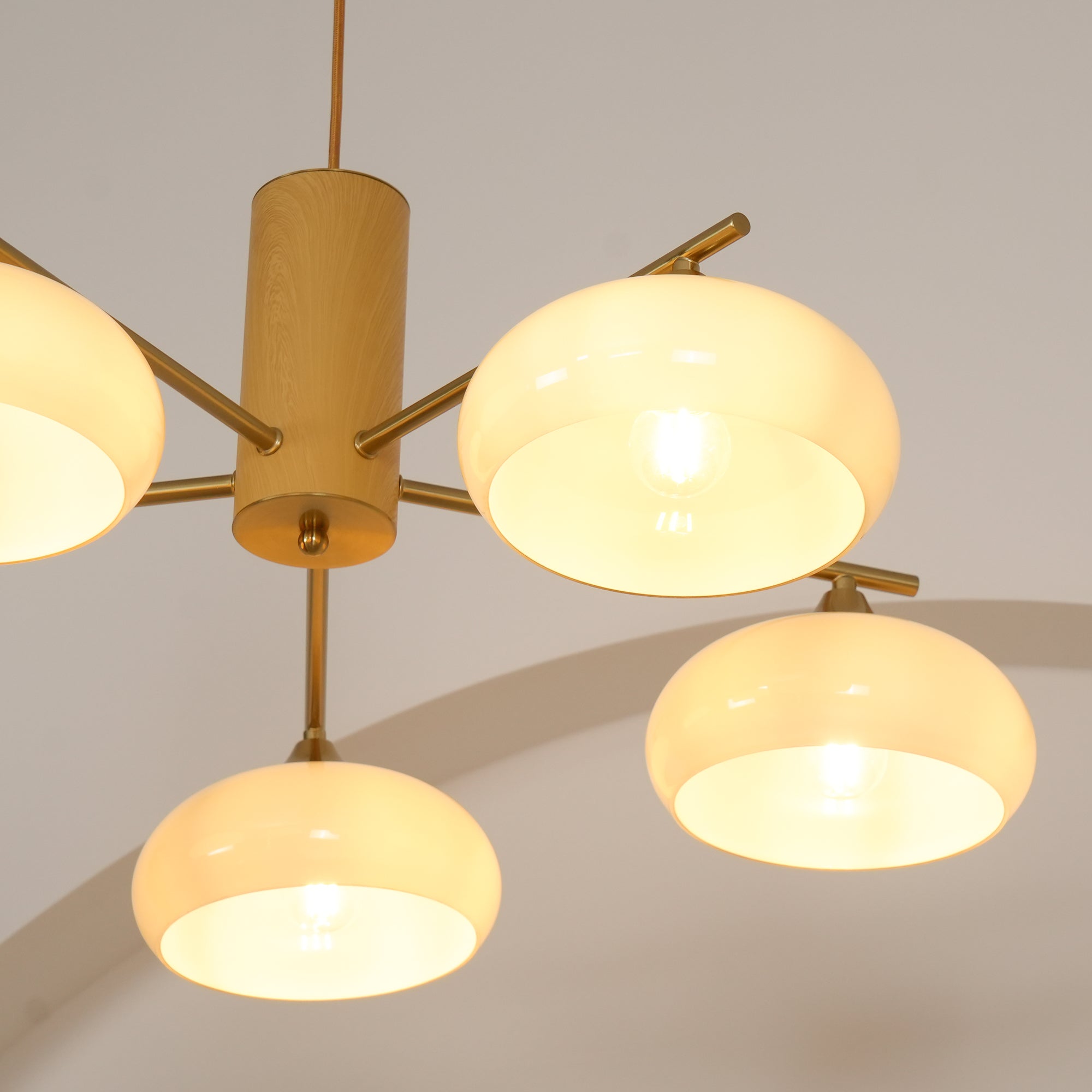 Detail of the Clérachic chandelier's brass cone fitters and wood body with five beige shades lit around it.