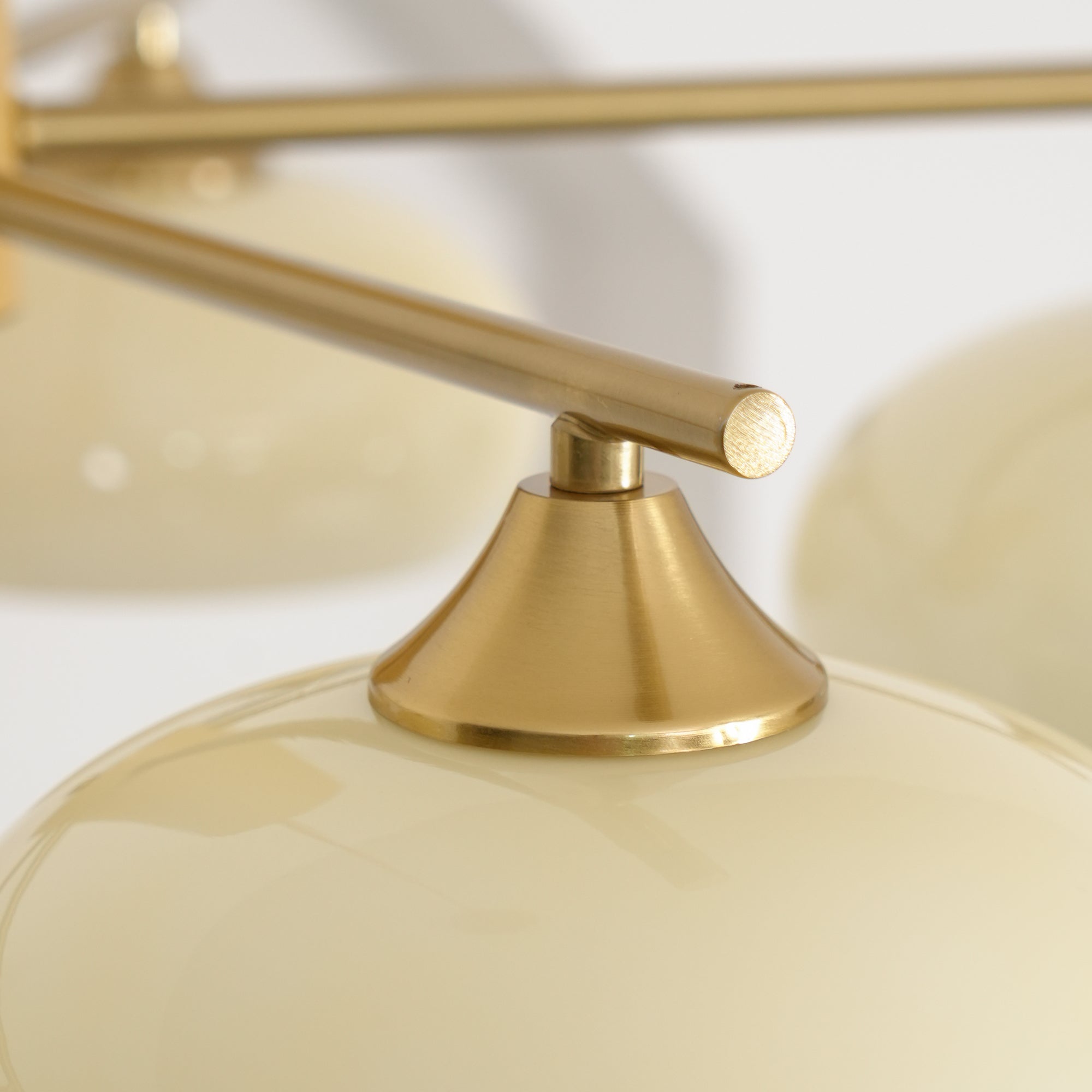 Macro of the brushed brass cone fitter meeting the glossy beige glass shade on the Clérachic chandelier.