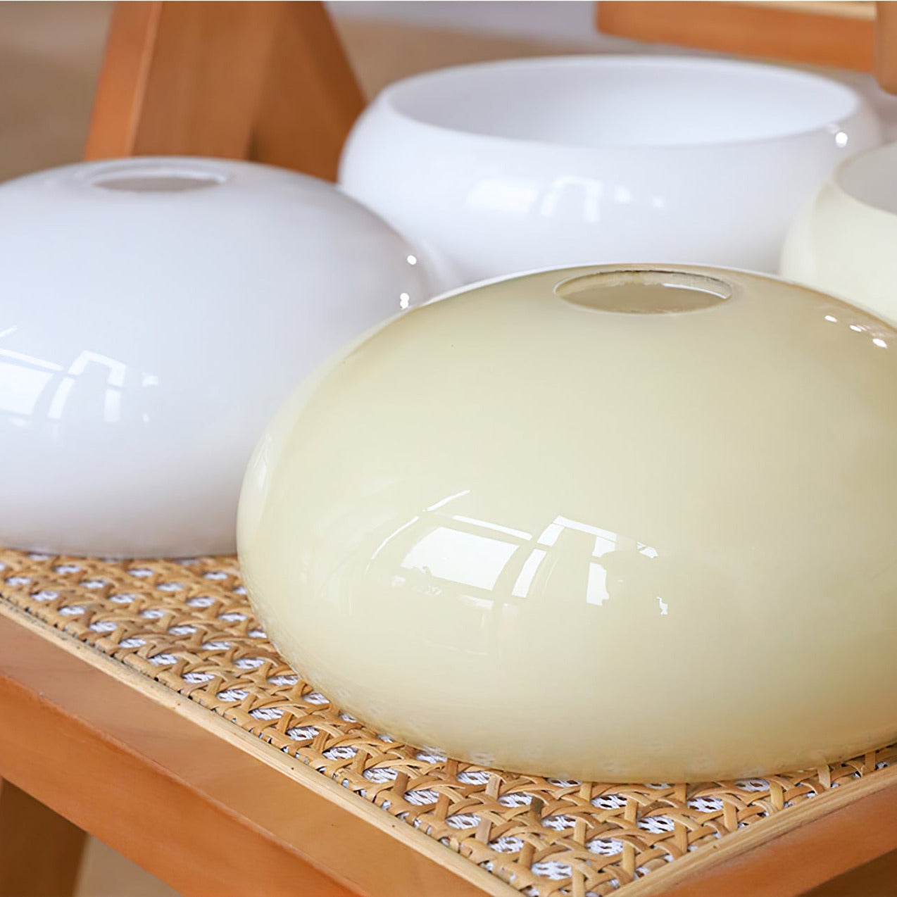 Spare Clérachic chandelier shades on a cane bench, two white and one beige, showing the top fitter hole.
