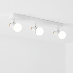 Clérachic white three-head ceiling spotlight bar with globe bulbs glowing, adjustable cone heads with wooden end caps.
