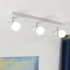 Clérachic white three-head ceiling spotlight bar with globe bulbs lit in a room with a landscape painting and blue curtain.