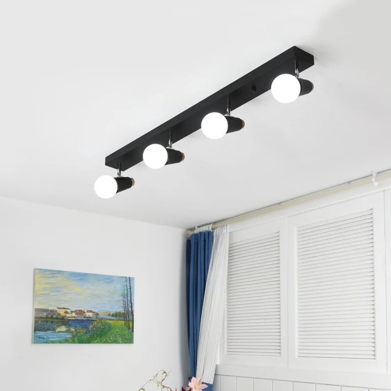 Clérachic black four-head ceiling spotlight bar with globe bulbs lit above a room with a landscape painting and shutters.