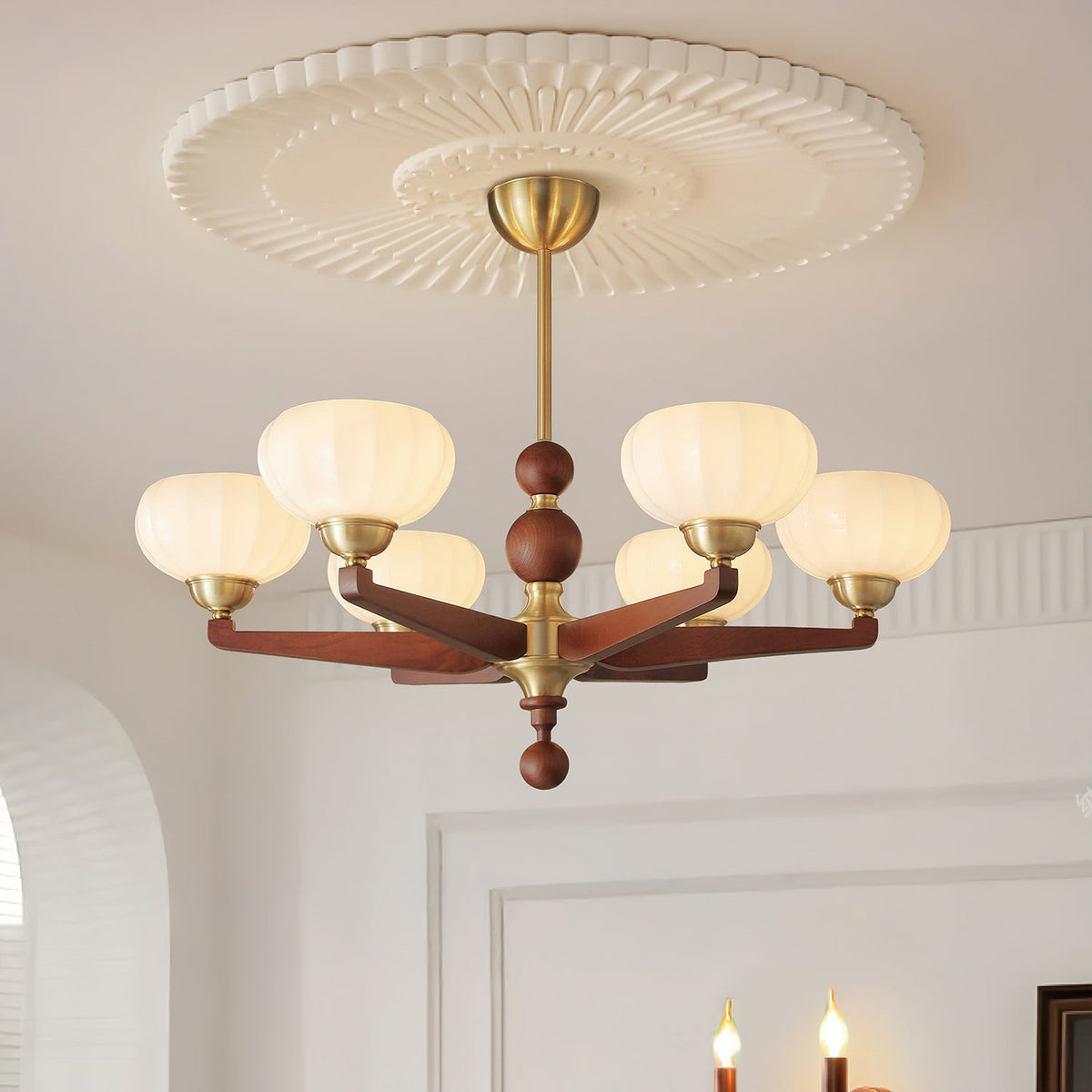Below a ribbed white ceiling rose, this Clérachic chandelier hangs from a brass stem, its cream glass shades lit in a bright white room.