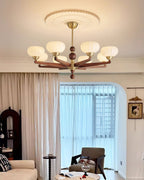 Wide view of a living room with a Clérachic chandelier lit overhead, above a sofa, an armchair and sheer curtains at the window.