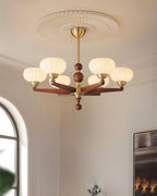 Cream glass shades on this Clérachic chandelier, lit below a ribbed ceiling rose, with an arched window at the edge of the frame.