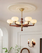 This Clérachic chandelier hangs close to a ribbed ceiling rose, with a candle-style wall light and a leafy plant in the room below.
