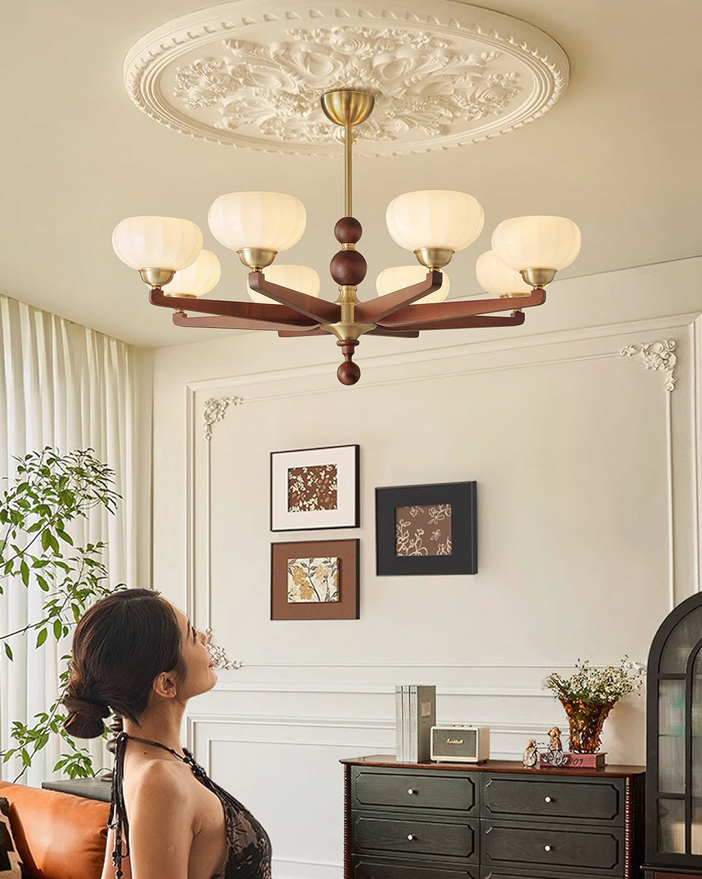 Looking up at this Clérachic chandelier, with a person beside it in a room of panelled walls, framed prints and a dark chest of drawers.