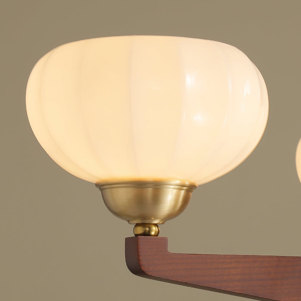 Close view of a ribbed cream glass shade on this Clérachic chandelier, seated in a brass cup on a wood arm.