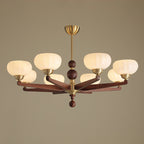 The widest form of this Clérachic chandelier, with eight cream glass shades on wood arms and a brass stem, against a taupe backdrop.