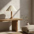 On a rough-hewn wooden console against a textured plaster wall, this Clérachic table lamp sits near a stone vase and a linen floor cushion.