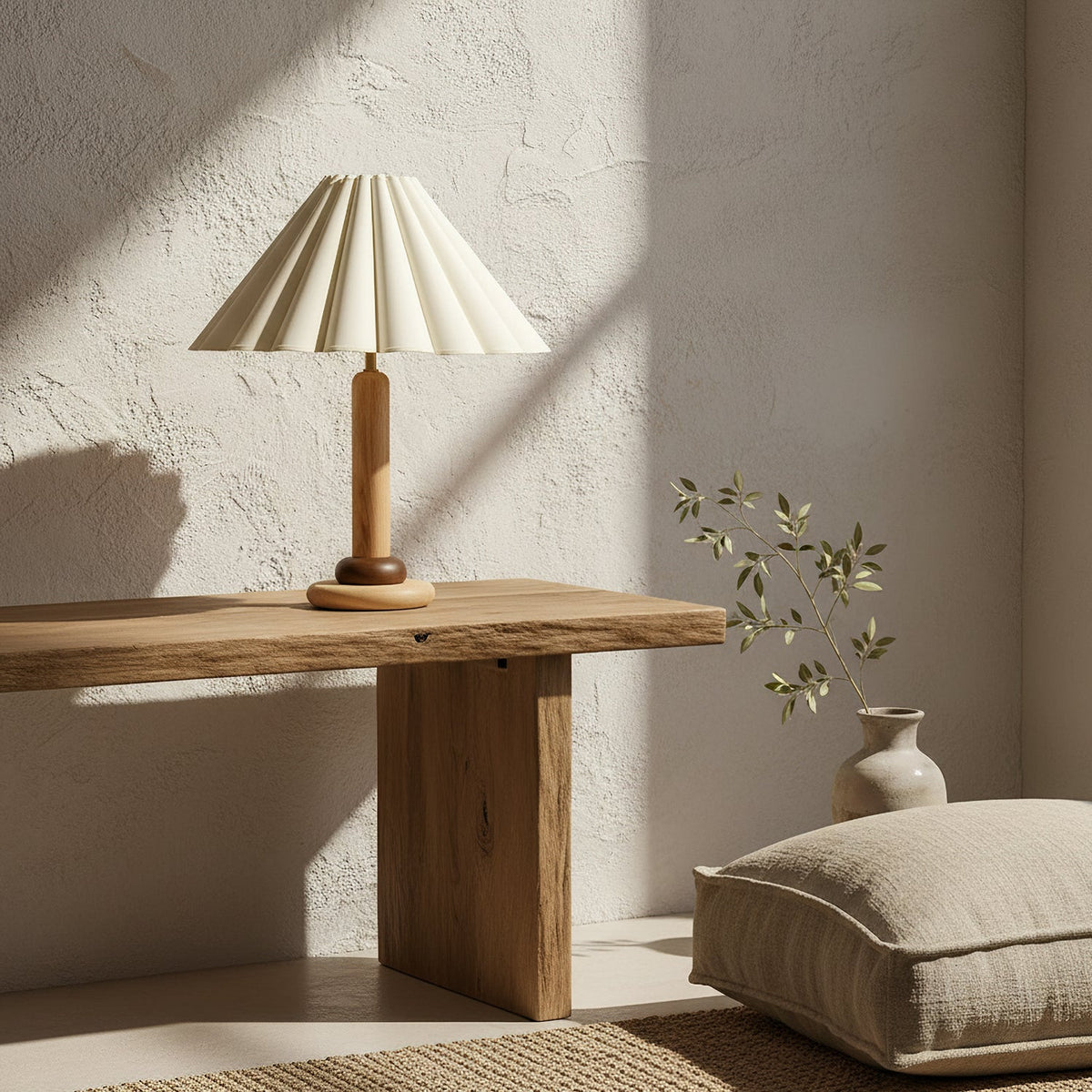 On a rough-hewn wooden console against a textured plaster wall, this Clérachic table lamp sits near a stone vase and a linen floor cushion.