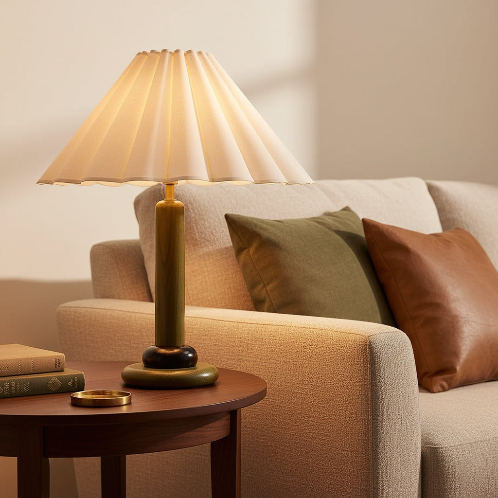 A lit Clérachic table lamp with an olive-green wooden stem glows beside a cream sofa with green and tan cushions and a round side table.