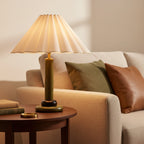 A lit Clérachic table lamp with an olive-green wooden stem glows beside a cream sofa with green and tan cushions and a round side table.