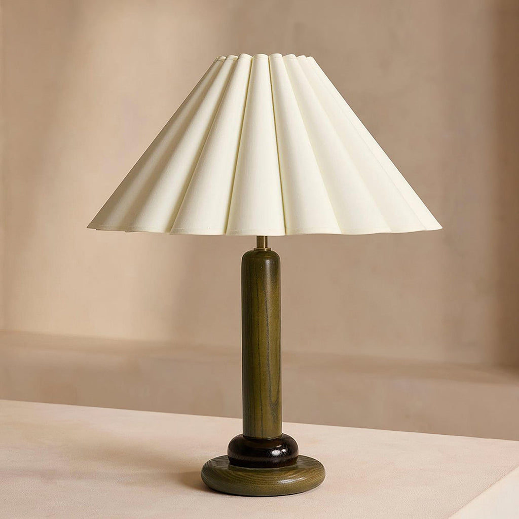 Close view of this Clérachic table lamp with a deep green wooden stem, a dark ring and a wide pleated cream shade.