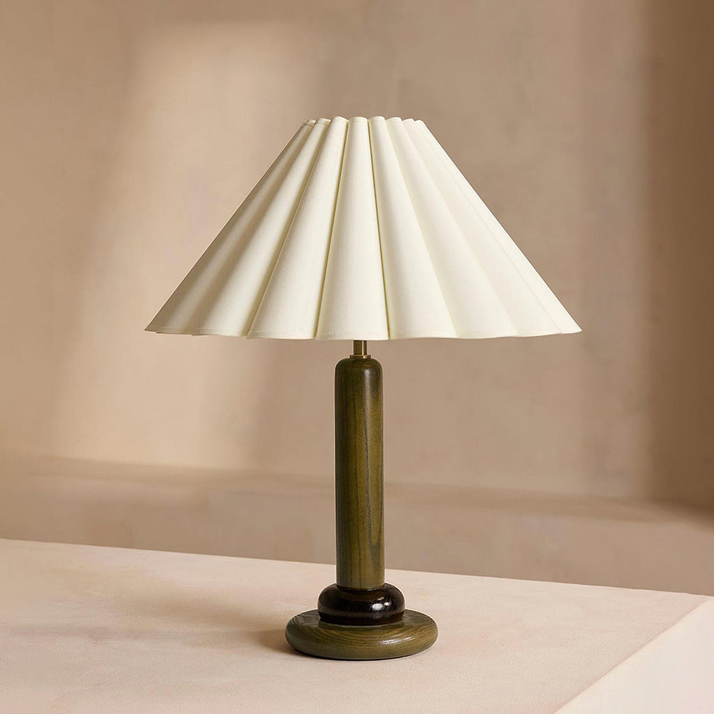 Straight-on view of this Clérachic table lamp with a dark green stem and base, on a pale surface against a warm beige wall.