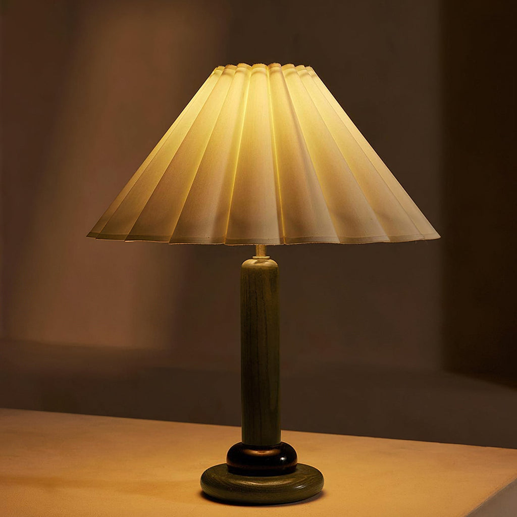 Seen close up and lit, this Clérachic table lamp with a green wooden stem casts a golden glow through its pleated shade.