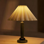 Seen close up and lit, this Clérachic table lamp with a green wooden stem casts a golden glow through its pleated shade.