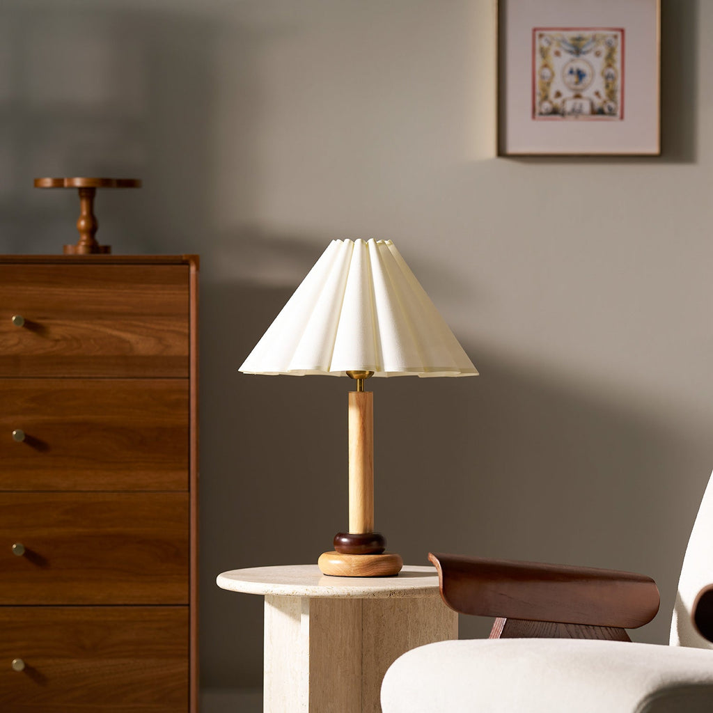 A Clérachic natural wood table lamp stands on a round travertine side table, with a walnut chest of drawers and a framed print behind.