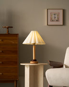 A smaller view of this Clérachic wood table lamp on a pale stone side table, with a framed print and tall chest of drawers beyond.