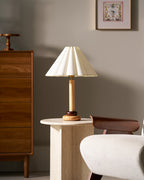 This Clérachic wood-stemmed table lamp stands on a stone side table, with a walnut chest of drawers and a cream armchair to the right.