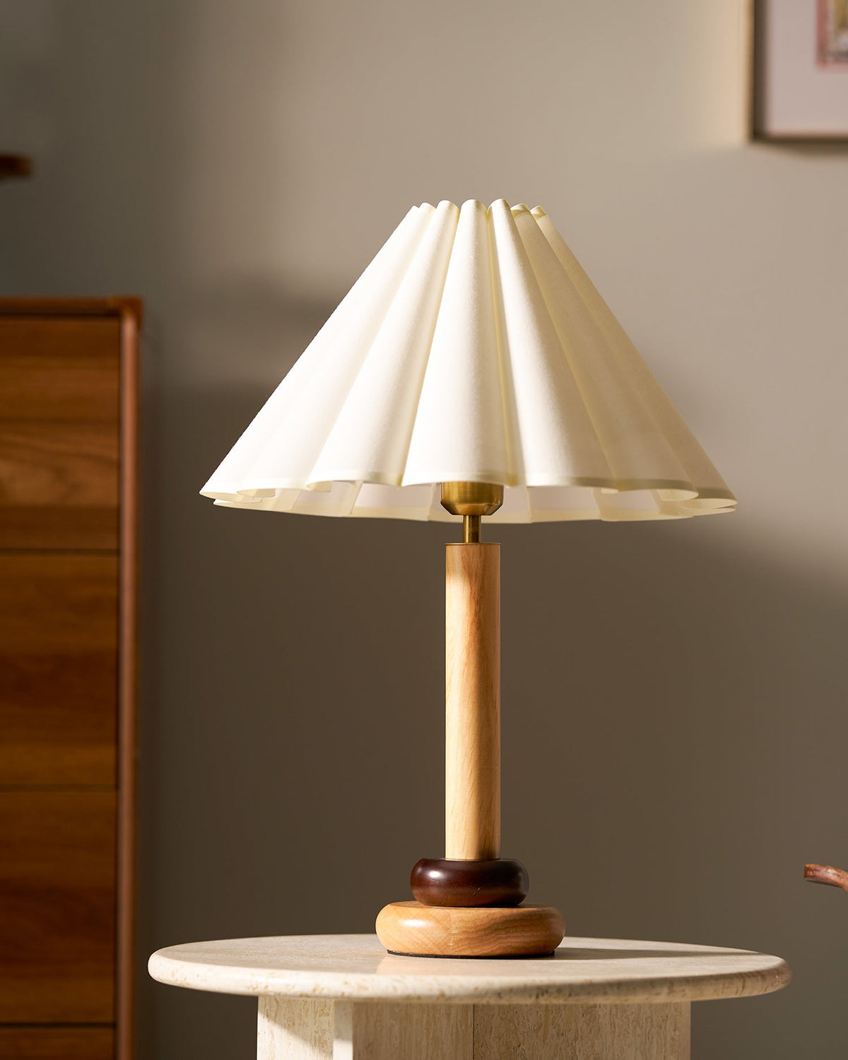 Close view of this Clérachic table lamp's pleated cream shade and natural wood stem, on a stone table before a wood-panelled wall.