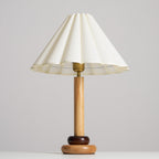 A Clérachic table lamp with a natural wood stem, a brass fitting and a wide scalloped cream shade against a pale grey backdrop.