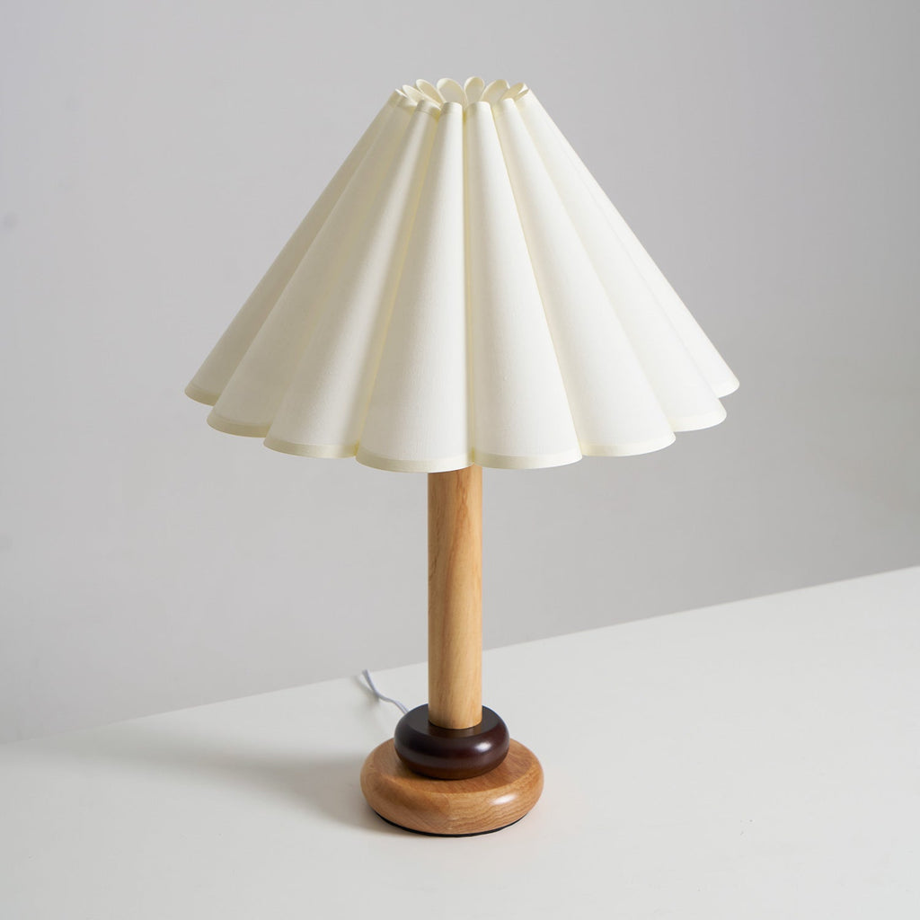 This Clérachic natural wood table lamp stands on a white surface, with a dark ring above its round base and a scalloped shade.