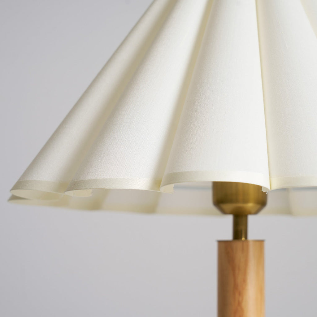 Close view of the scalloped hem of the pleated cream fabric shade and the brass fitting on this Clérachic table lamp.
