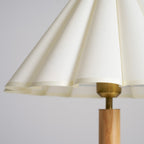 Close view of the scalloped hem of the pleated cream fabric shade and the brass fitting on this Clérachic table lamp.