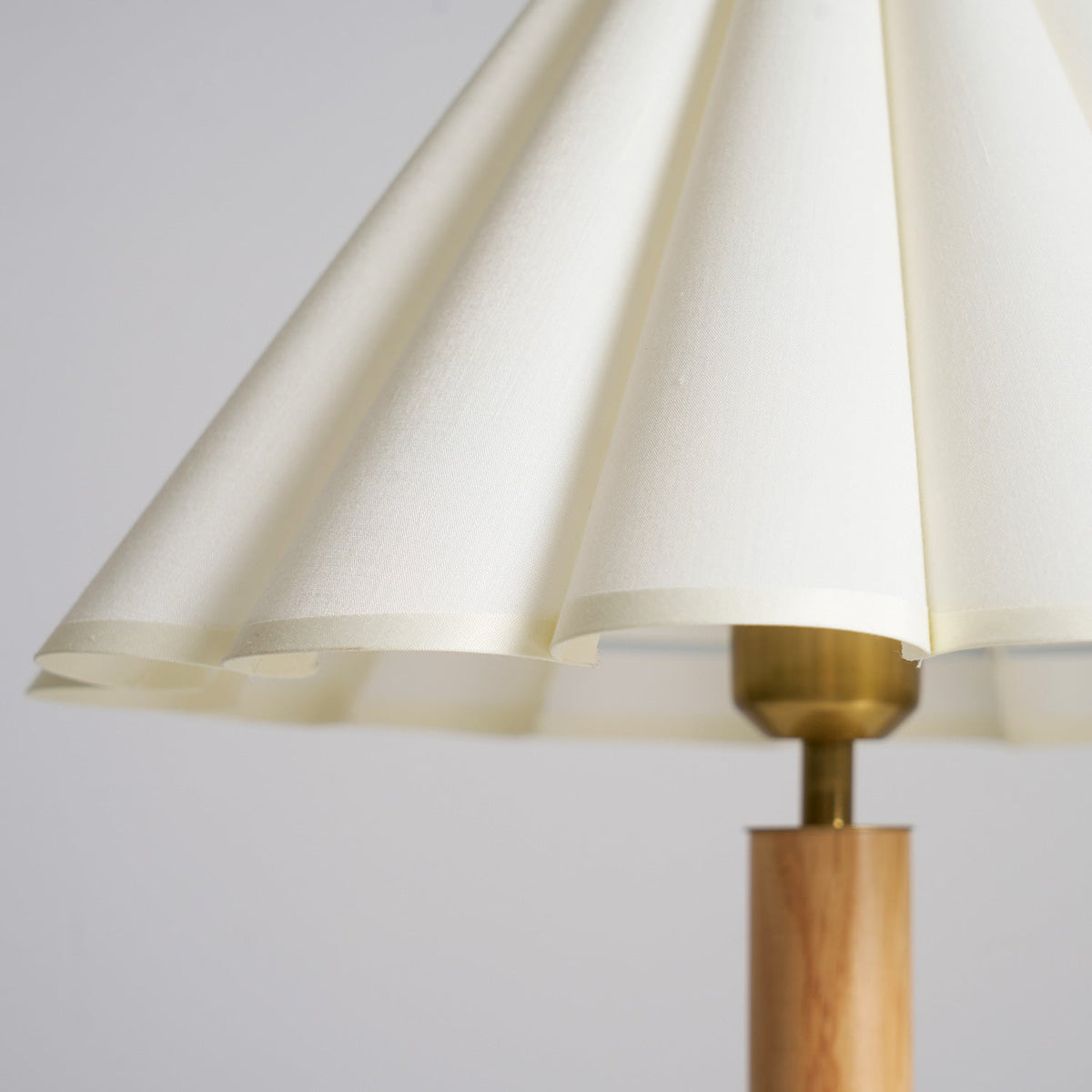 Close view of the scalloped hem of the pleated cream fabric shade and the brass fitting on this Clérachic table lamp.
