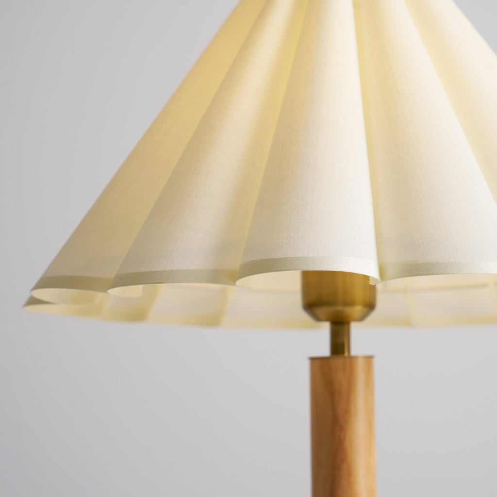 Close view of the pleats, scalloped edge and brass collar where the shade meets the wooden stem on this Clérachic lamp.