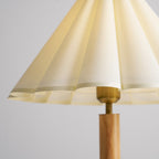 Close view of the pleats, scalloped edge and brass collar where the shade meets the wooden stem on this Clérachic lamp.