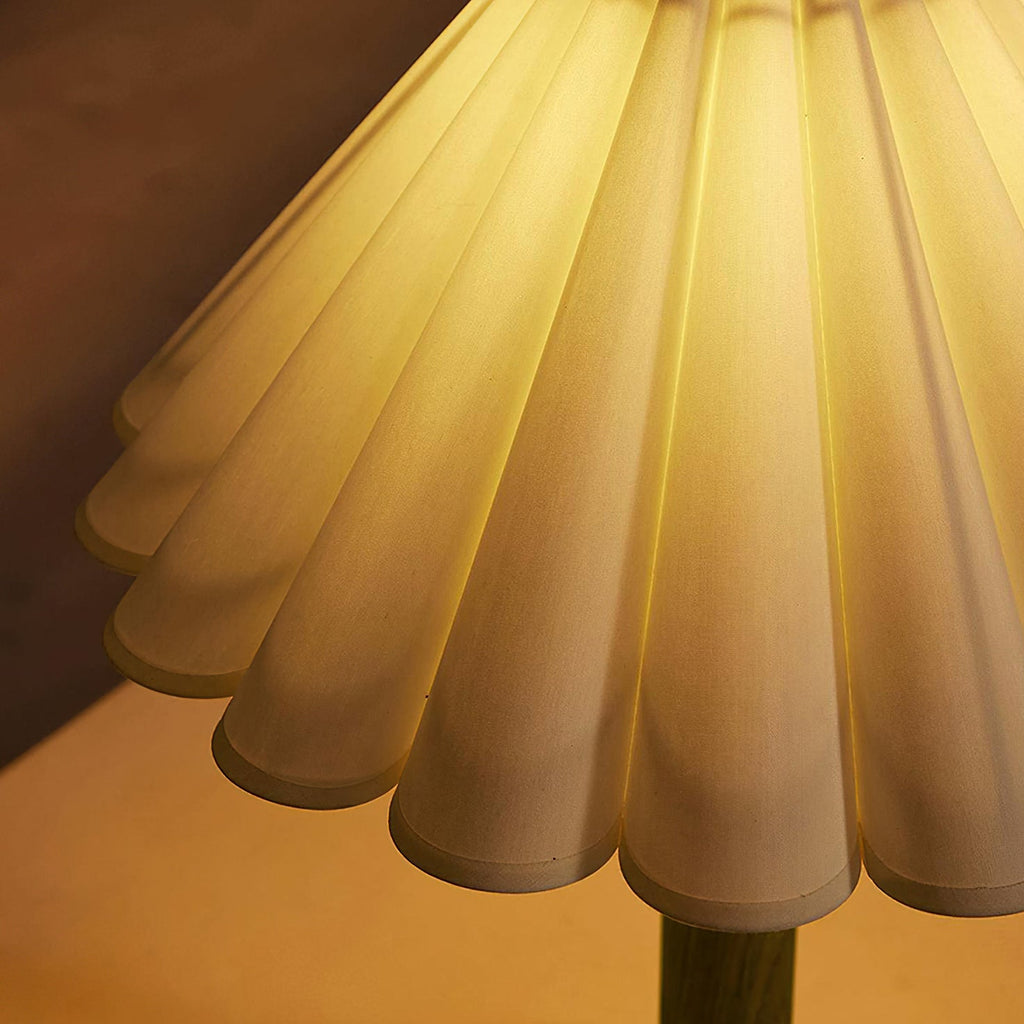 Close view of the glowing scalloped lower edge of the pleated shade on this Clérachic table lamp, lit warmly from inside.