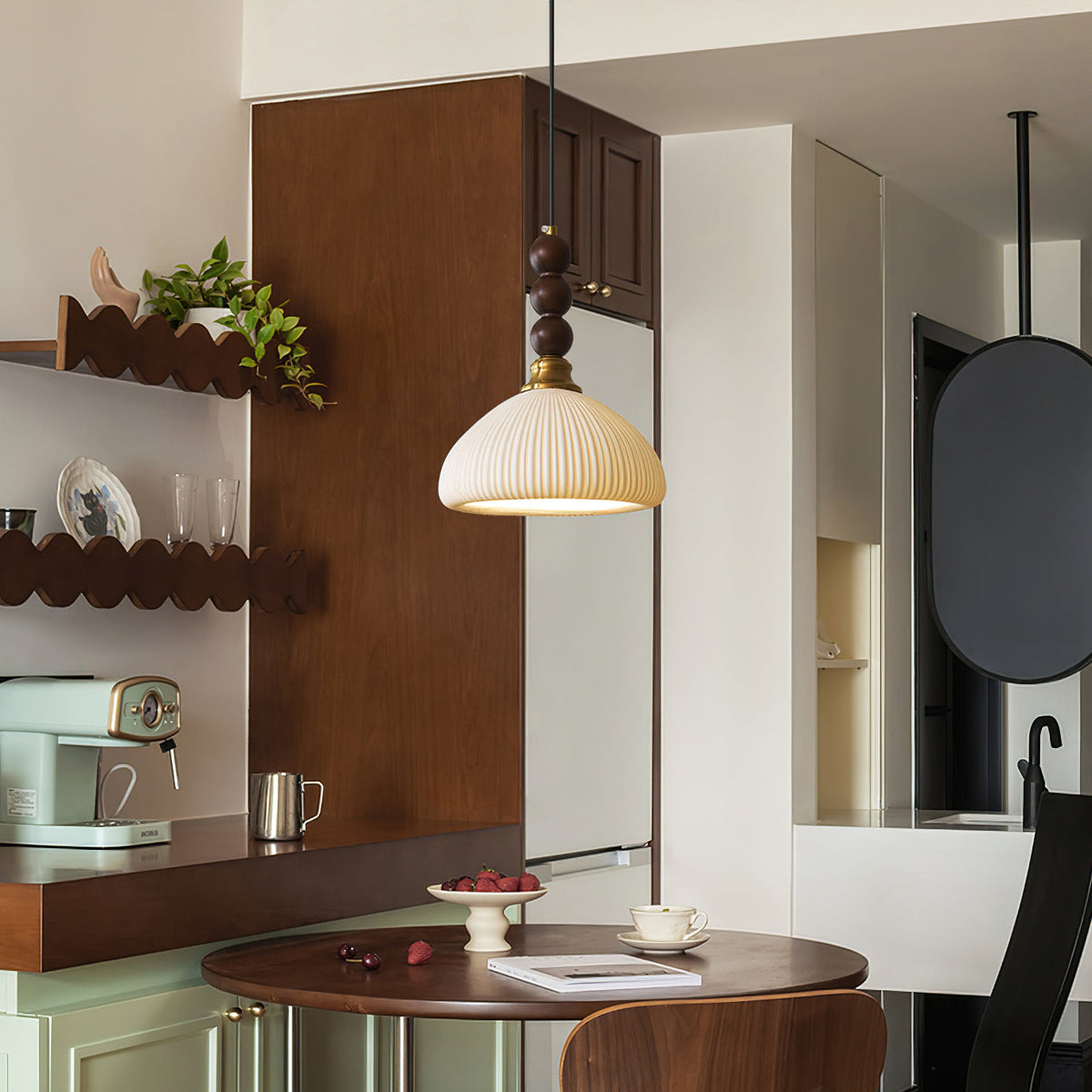 Above a round walnut table in a small dining corner, this Clérachic pendant glows with a ribbed ceramic shade.