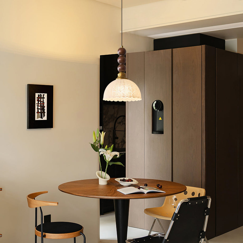 Wider view of a Clérachic pendant with a small scalloped shade above a round walnut table and black-and-tan chairs.
